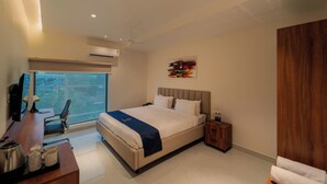 Habitación de hotel moderna con una cama grande, un escritorio con silla, una mesita de noche de madera y una ventana con vistas.