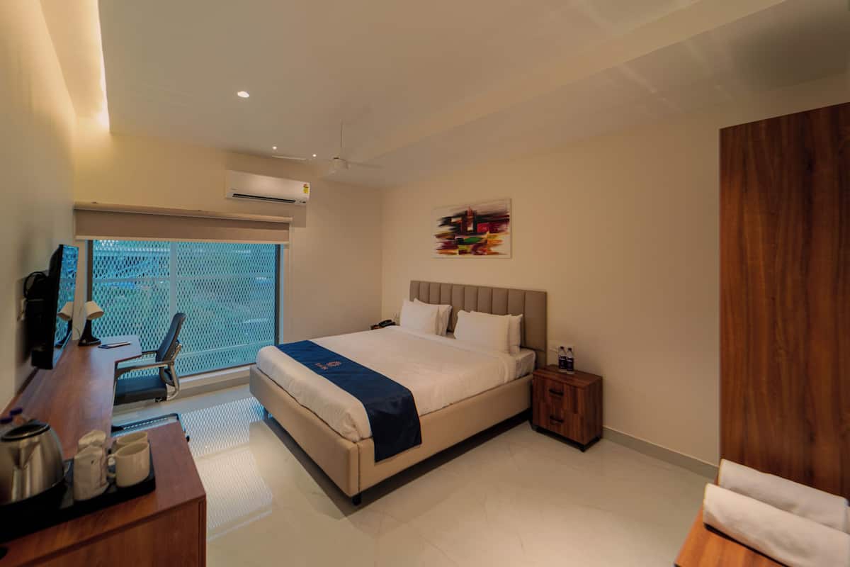Habitación de hotel moderna con una cama grande, un escritorio con silla, una mesita de noche de madera y una ventana con vistas.