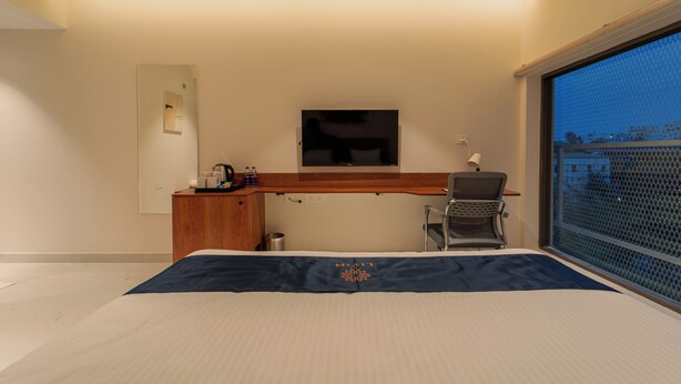 Habitación de hotel con cama, escritorio, silla, televisor montado en la pared y ventana con vista a la ciudad.