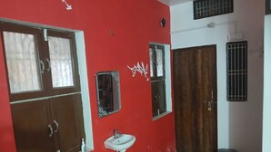 A room with a red wall, a white sink, and a wooden door. - Kaashvi Home Stay (Varanasi)