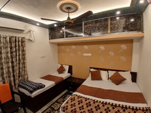 A hotel room with two single beds, a ceiling fan, a patterned headboard, and a small table. - Kaashvi Home Stay (Varanasi)