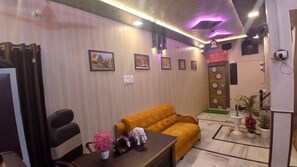 A room with a sofa, a table with decorative items, a wall-mounted TV, and framed pictures. - Kaashvi Home Stay (Varanasi)