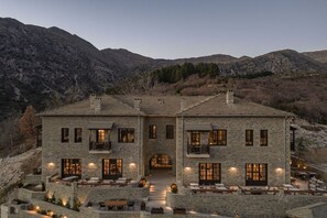 Un edificio de piedra de dos pisos con un patio, ventanas grandes y mesas al aire libre.
