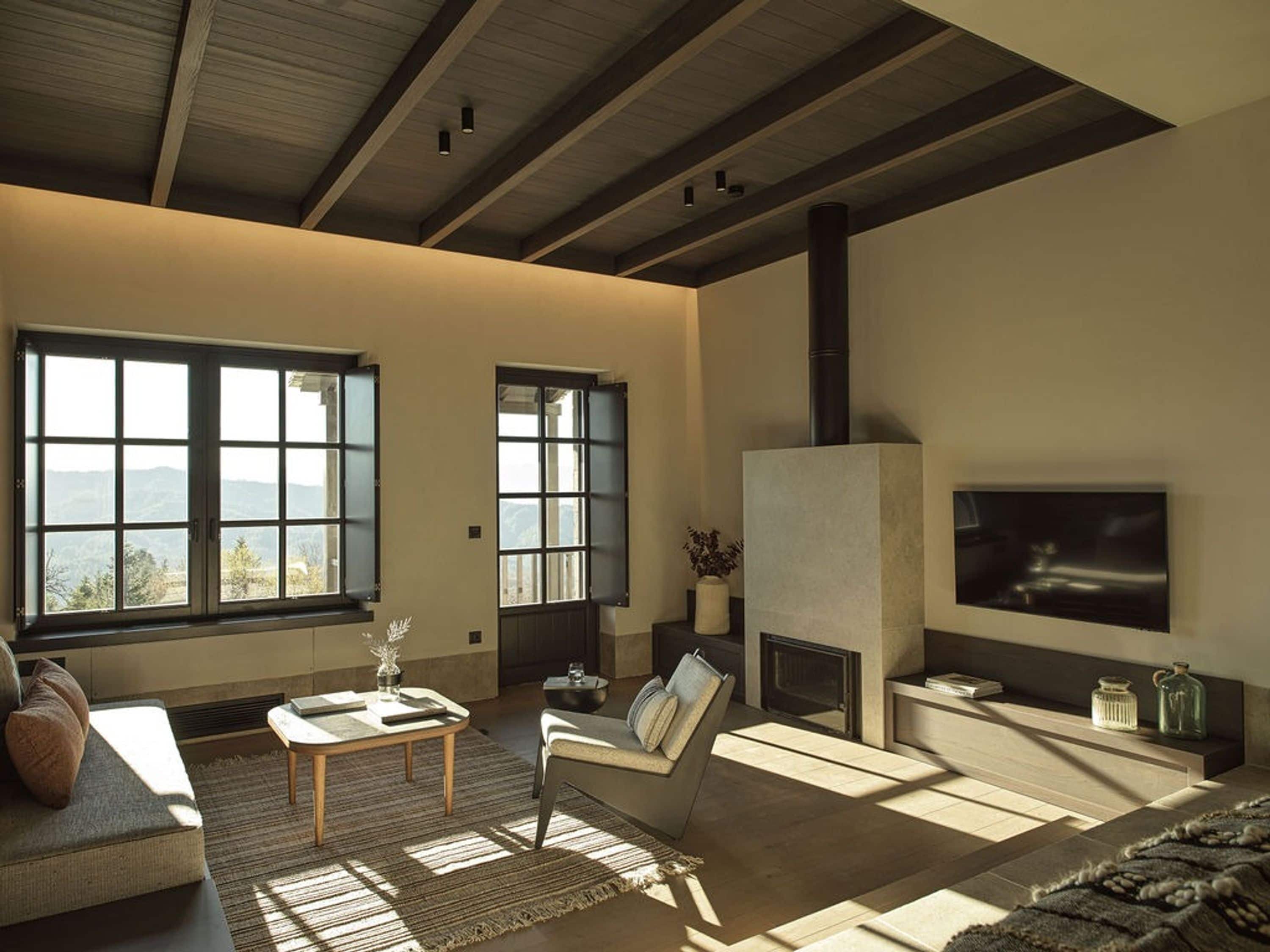 A spacious living room with large windows, a fireplace, and a television mounted on the wall.
