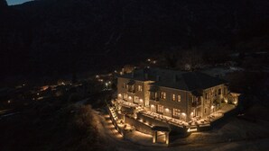 A large, well-lit hotel with multiple floors and a spacious outdoor area, surrounded by mountains. - Oreno Mountain Retreat Hotel (Zagori)