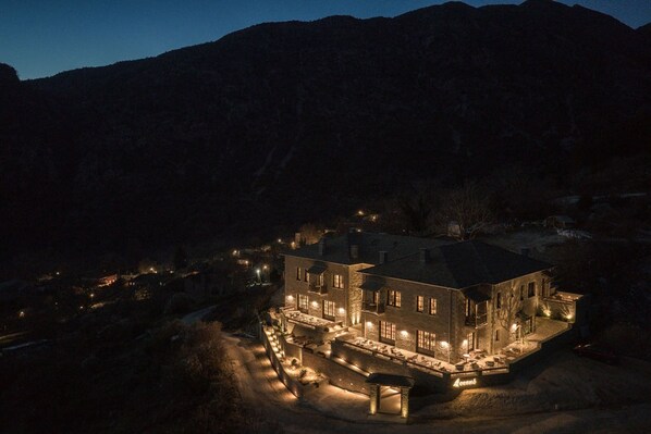 A large, well-lit hotel with multiple floors and a spacious outdoor area, surrounded by mountains. - Oreno Mountain Retreat Hotel (Zagori)
