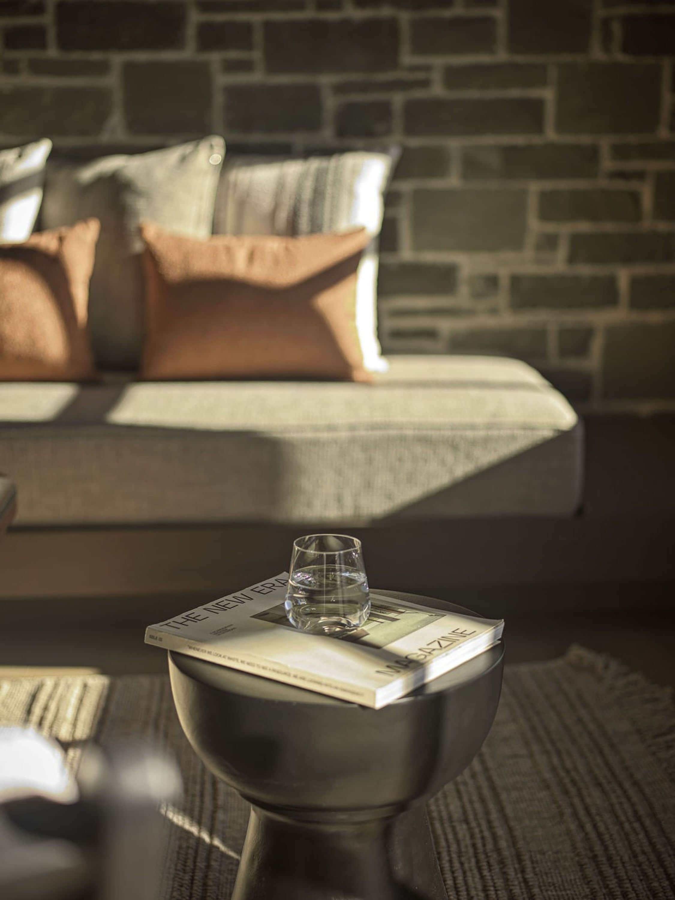 A modern living room with a sofa, pillows, a coffee table with a magazine and a glass of water.