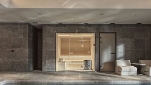 A modern indoor swimming pool with clear water, a sauna area, and a seating area with a sofa and armchairs. - Oreno Mountain Retreat Hotel (Zagori)