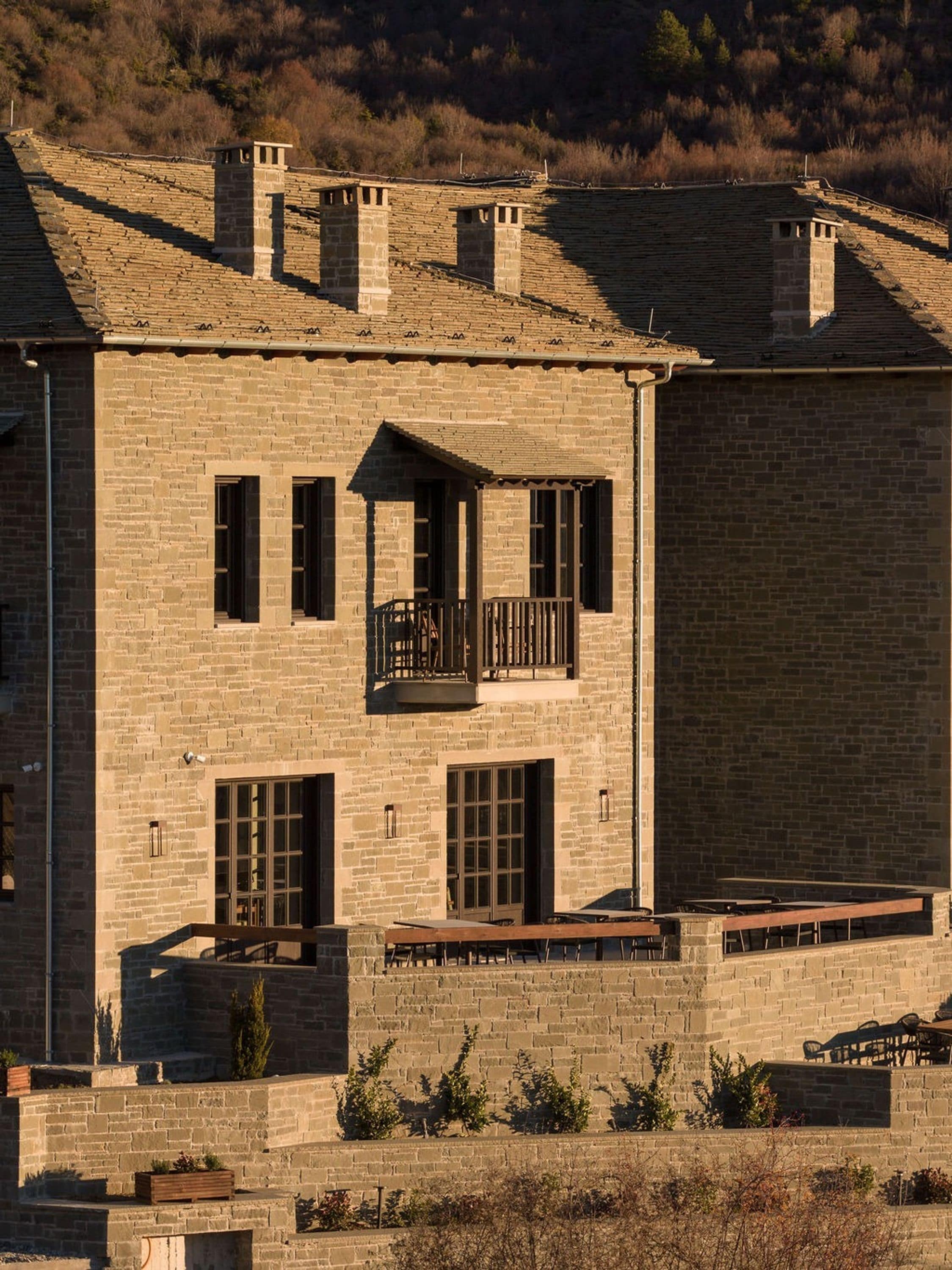 A stone building with a balcony, large windows, and a flat roof.