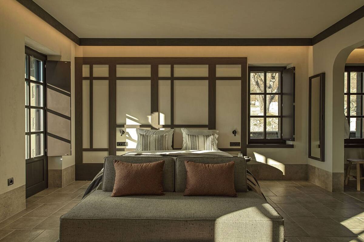 A bedroom with a large bed, a sofa, and a view of the outdoors through large windows.