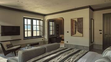 Une chambre d’hôtel moderne dotée d’un grand lit, d’un coin salon avec un canapé et des fauteuils, d’un téléviseur à écran plat fixé au mur et d’une grande fenêtre offrant une vue sur l’extérieur.