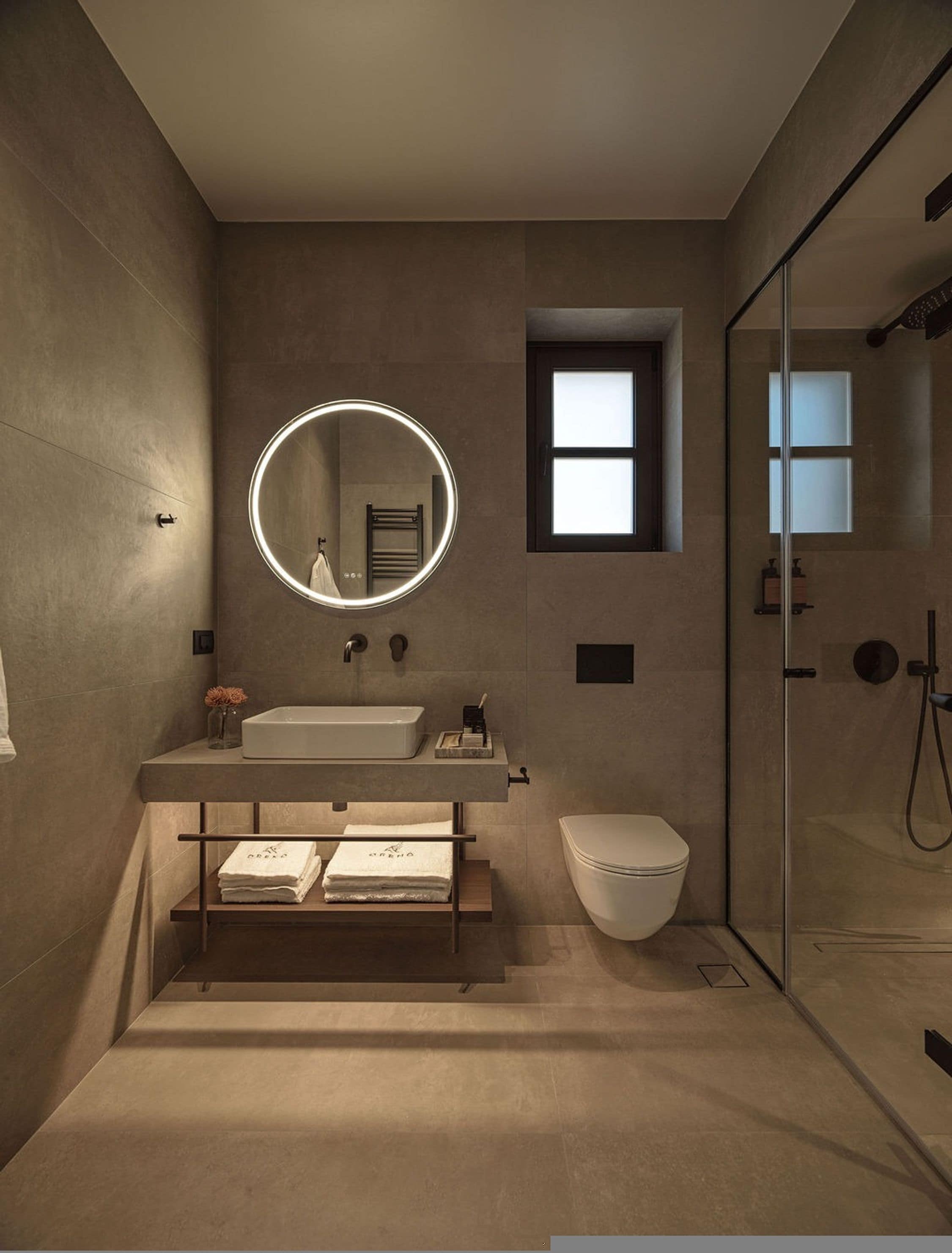 Een moderne badkamer met een ronde spiegel, een wastafel, een toilet en een douche met glazen wanden.