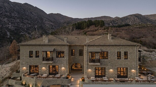 A two-story stone building with multiple windows, a central entrance, and outdoor seating areas.