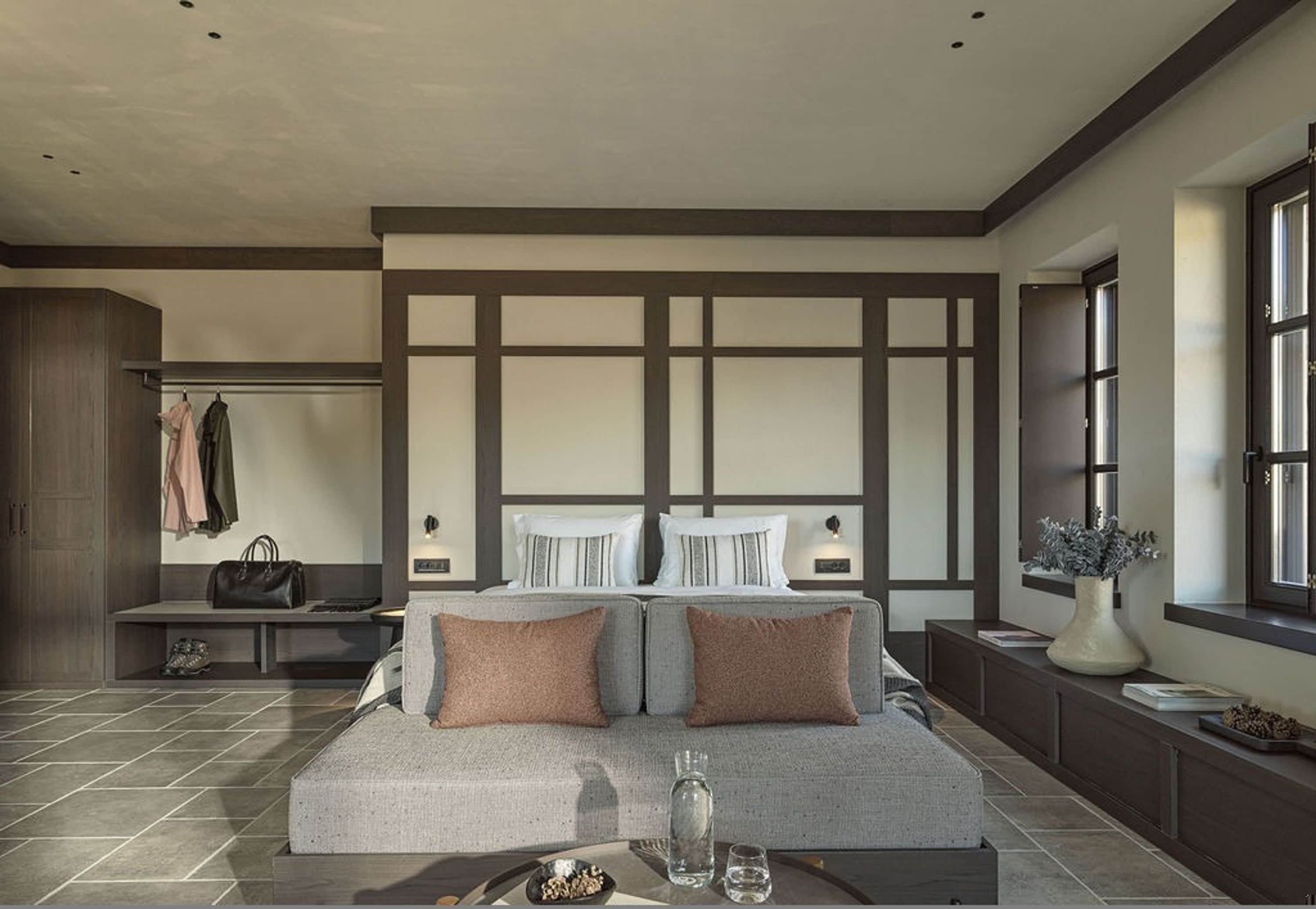 Un dormitorio moderno con una cama grande, un banco con ropa, un florero y una ventana.