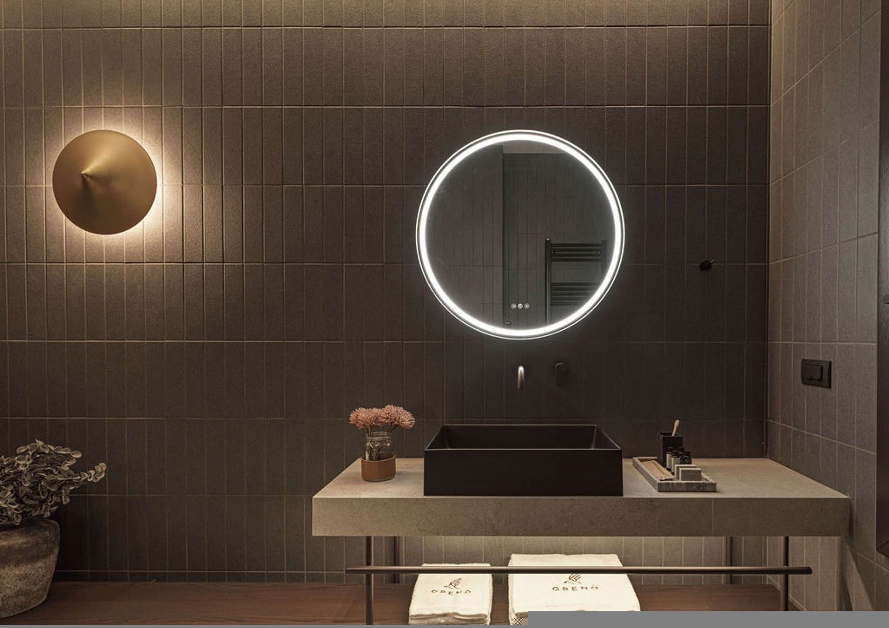 A modern bathroom with a round mirror, a sink, and a potted plant.