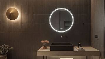A modern bathroom with a round mirror, a sink, and a potted plant.