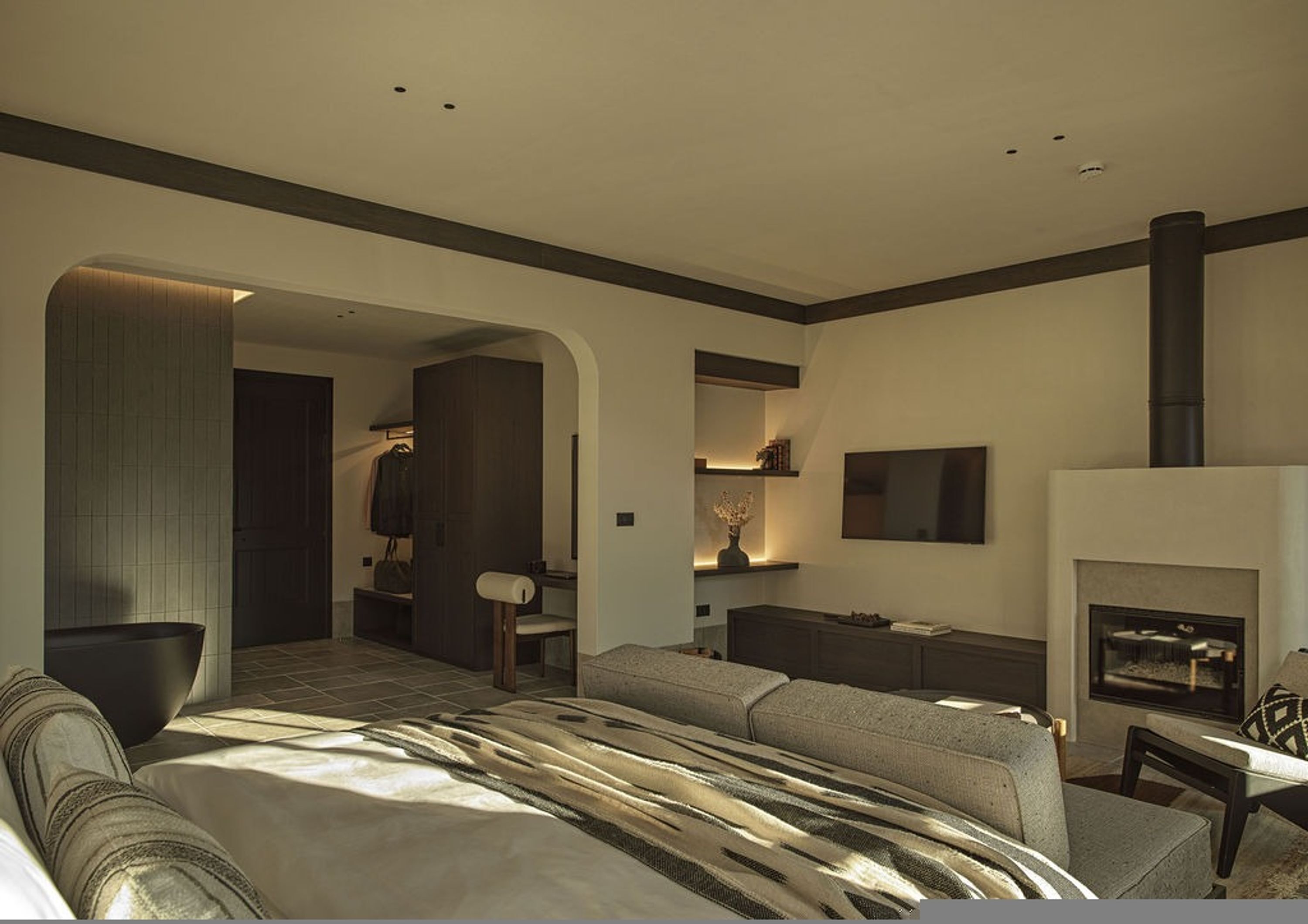 Una habitación de hotel moderna con una cama grande, una chimenea, un televisor y un vestidor.