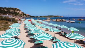 A beach with rows of green and white striped umbrellas and lounge chairs.