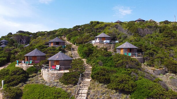 A hillside with several small, round-roofed buildings, each with a balcony and a stone pathway leading to them.