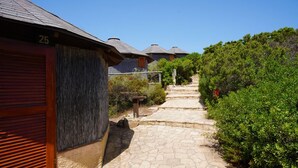 A stone pathway leading to traditional-style buildings with sloped roofs, surrounded by greenery.