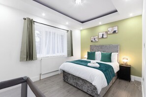 A modern bedroom with a bed, nightstand, and artwork on the wall. - 4 Bed - Sleeps 9 - Free Parking - 20 min Gatwick (Coulsdon)