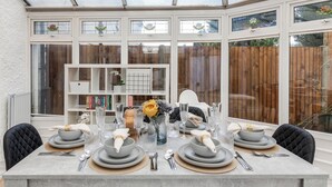 Zona pranzo in una veranda con un tavolo apparecchiato per sei, circondata da scaffali di libri e un recinto di legno.