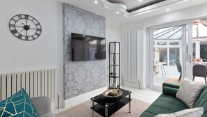 Un soggiorno moderno con una TV a schermo piatto, una sveglia decorativa e un divano verde.
