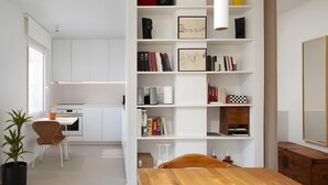 Une cuisine moderne avec des meubles blancs, une table à manger en bois et une bibliothèque contenant des livres et des objets décoratifs.