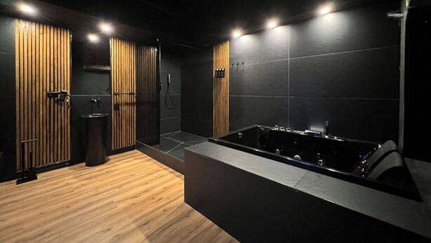 A modern bathroom with a wooden floor, a black bathtub, and a shower area. - Turin Central Cavour (Turin)