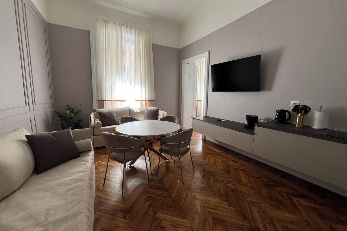 Una sala de estar moderna con un sofá, una mesa redonda para comer y un televisor de pantalla plana montado en la pared.