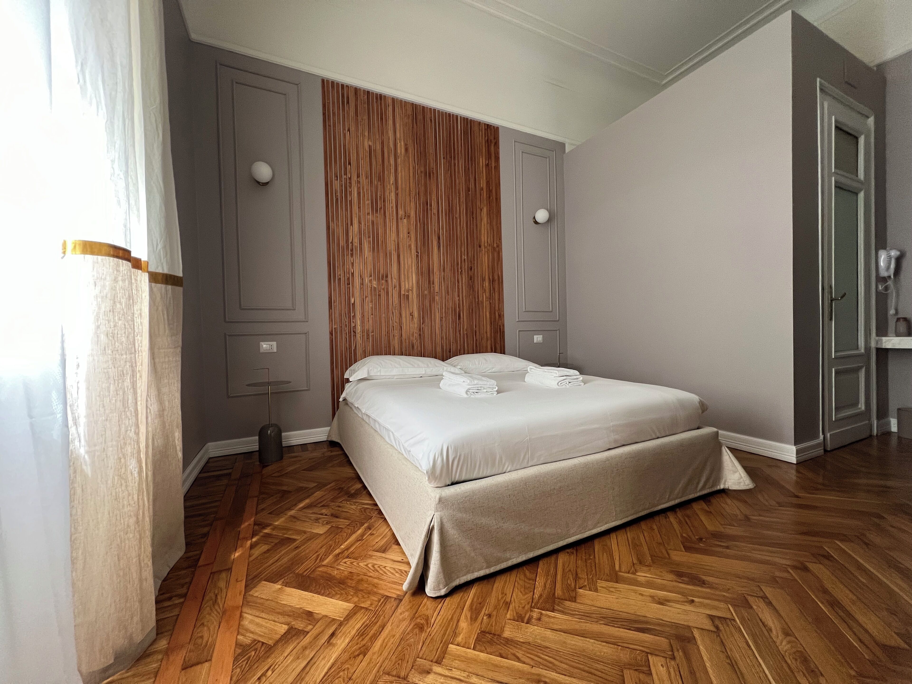 Ein Schlafzimmer mit Holzboden im Fischgrätmuster, einem Bett mit weißer Bettwäsche und einer Wandpaneele aus Holz.