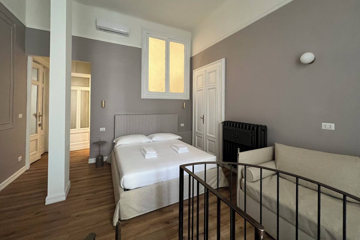Un dormitorio con cama, un radiador, una ventana, una puerta y una pared blanca.