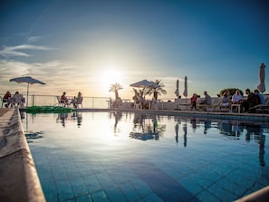 Ein Poolbereich mit Liegestühlen und Sonnenschirmen, umgeben von einem Zaun, mit Palmen im Hintergrund.