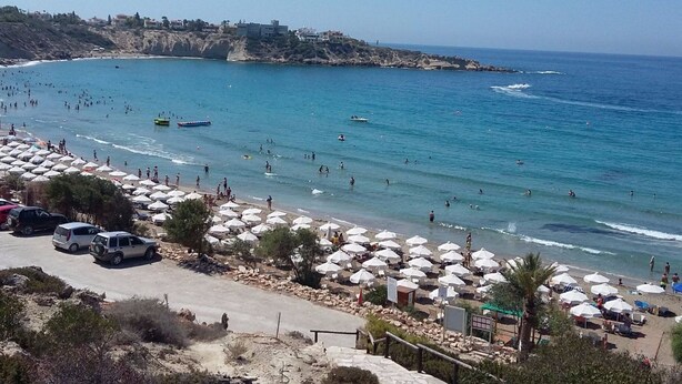 Una playa con numerosas sombrillas, un litoral rocoso y una vista despejada del mar.
