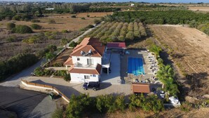 Una casa de dos pisos con piscina, rodeada de olivares y vistas al mar.
