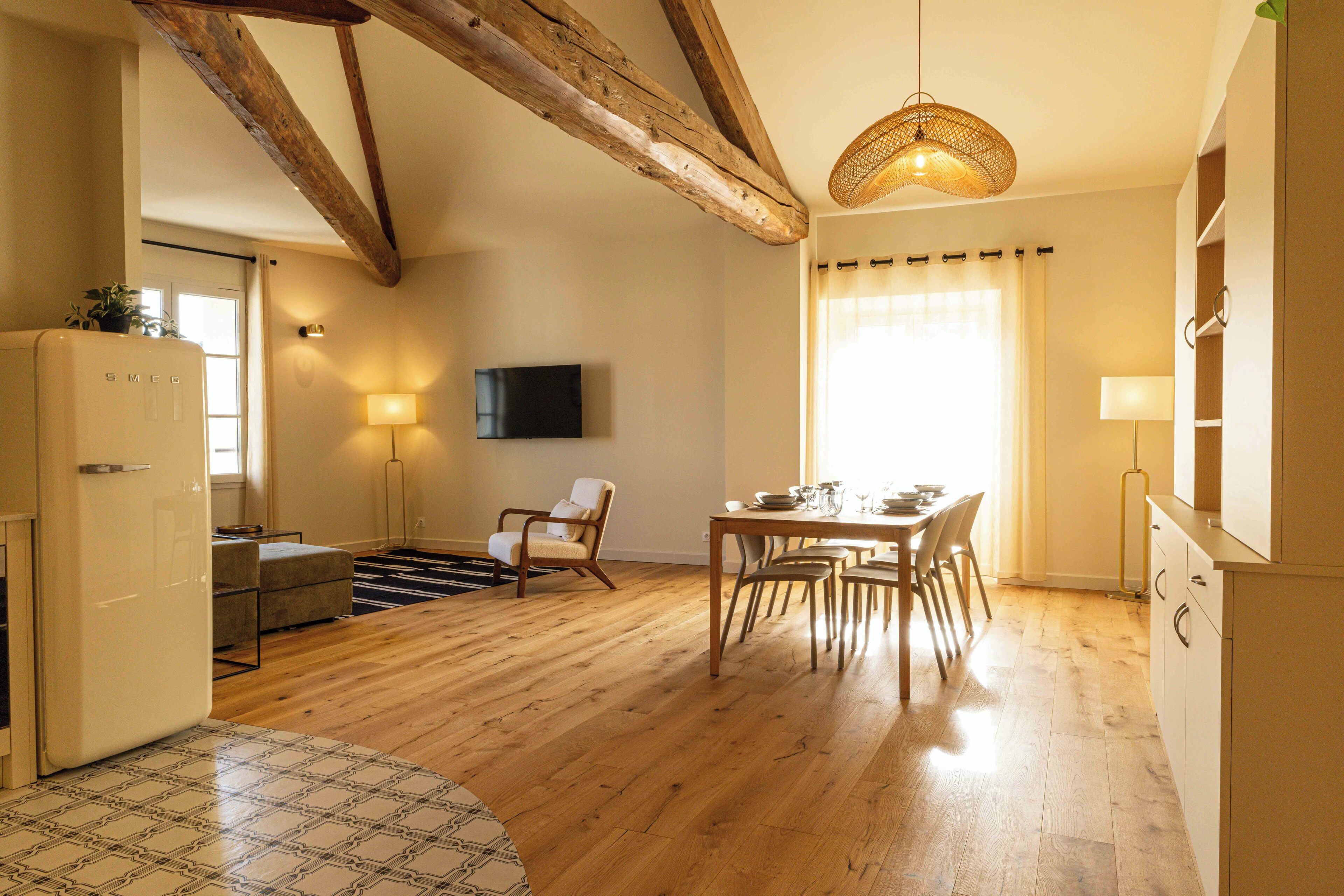 A spacious living area with wooden floors, a dining table, and a kitchen area with a refrigerator.