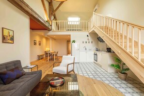 A spacious living area with a sofa, a dining table, and a white chair. A staircase leads to an upper level with a balcony. - OUSTAU DE MARIE (St.-Remy-de-Provence)