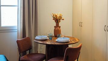 A small dining area with a round table, two chairs, a vase with flowers, and a window with curtains.