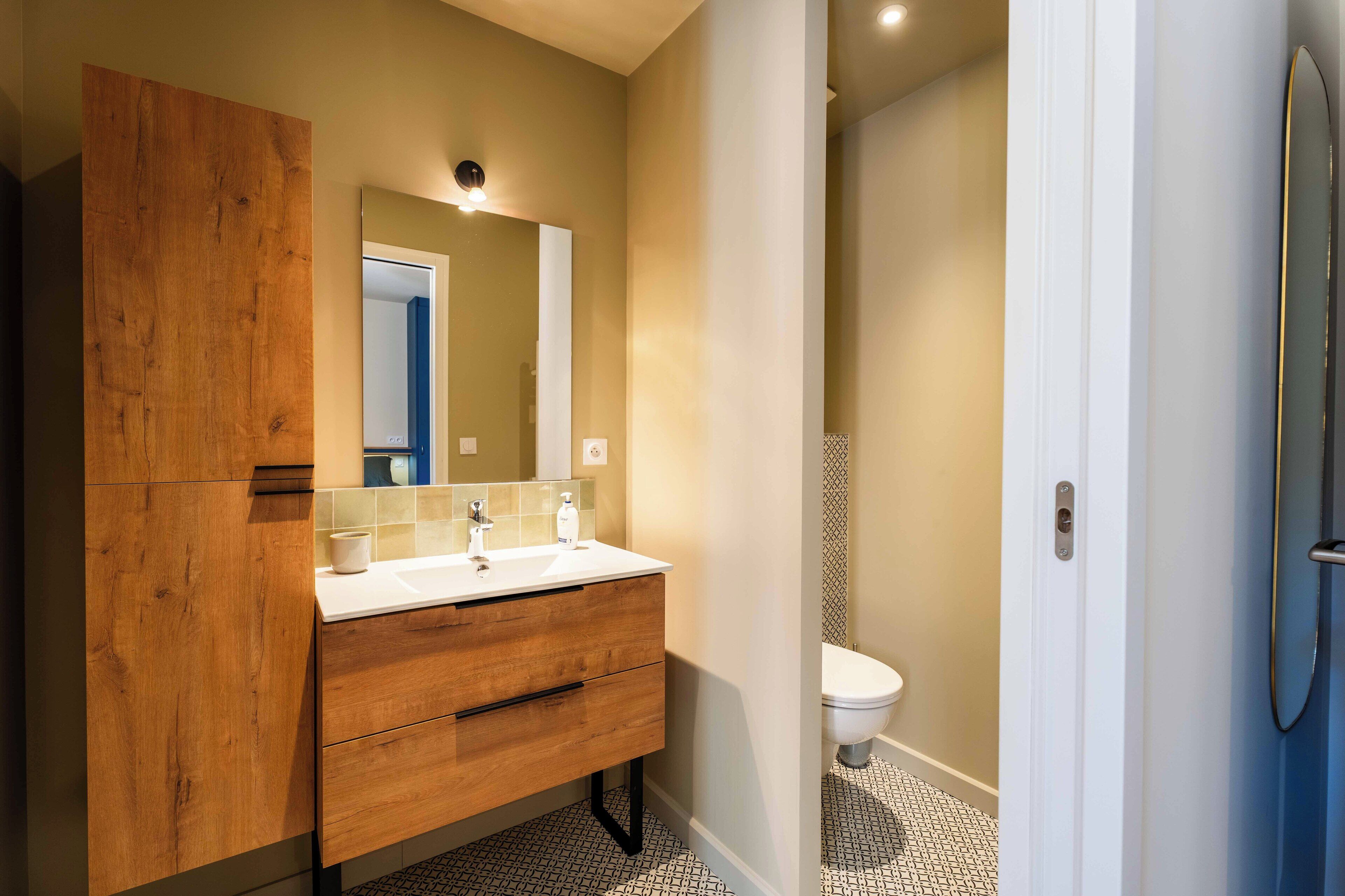 A modern bathroom with a wooden vanity, a white sink, and a mirror.