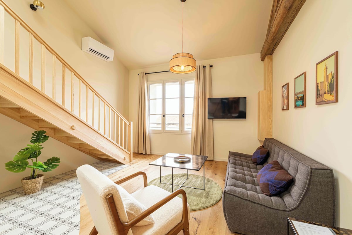 Ein Wohnzimmer mit Treppe, einer Couch, einem Sessel, einem Tisch und einem Fernseher.