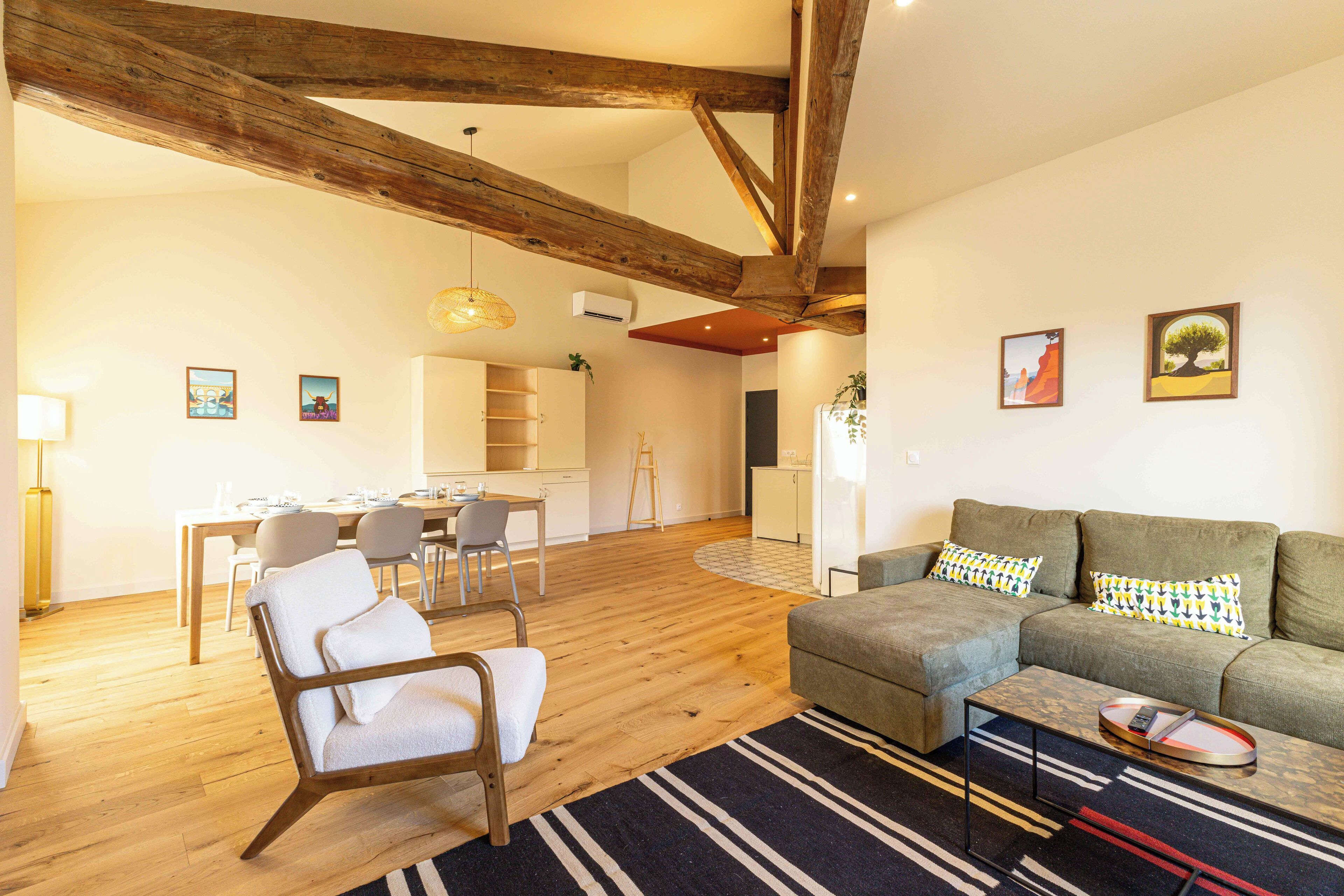 A modern living room with a wooden ceiling, a sofa set, a dining area, and a kitchen in the background.
