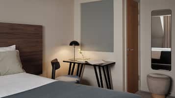 A neatly arranged hotel room with a bed, a desk with a lamp, a mirror, and a small stool.