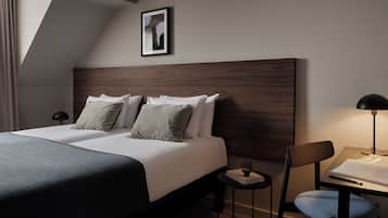 A modern hotel room with a large bed, a wooden headboard, a small table with a chair, and a framed picture on the wall.