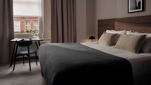 Une chambre d’hôtel avec un grand lit, un bureau avec une chaise, une lampe et une fenêtre avec des rideaux.