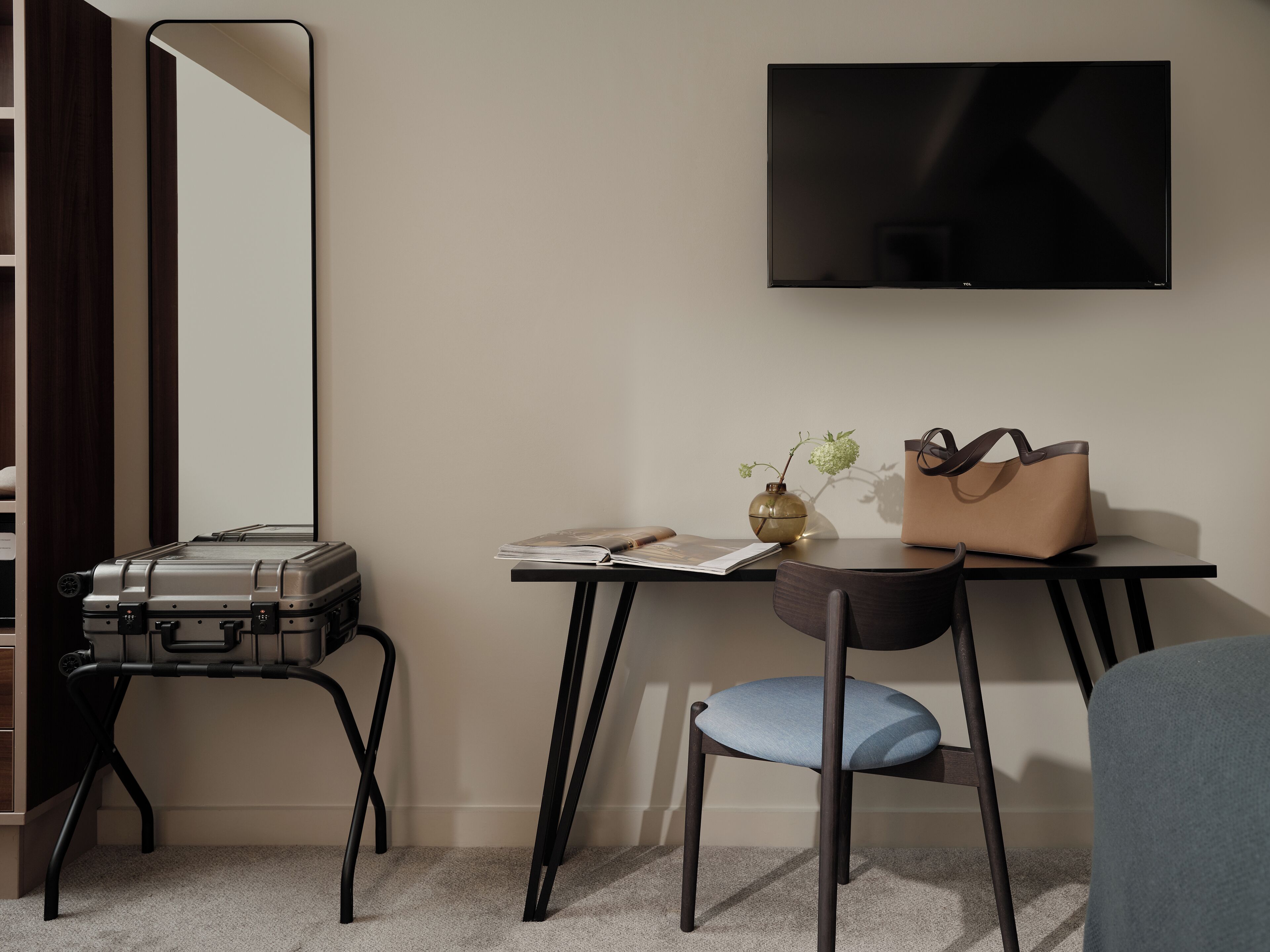 Hotelkamer met een bureau, een stoel, een koffer, een televisie en een vaas met bloemen.