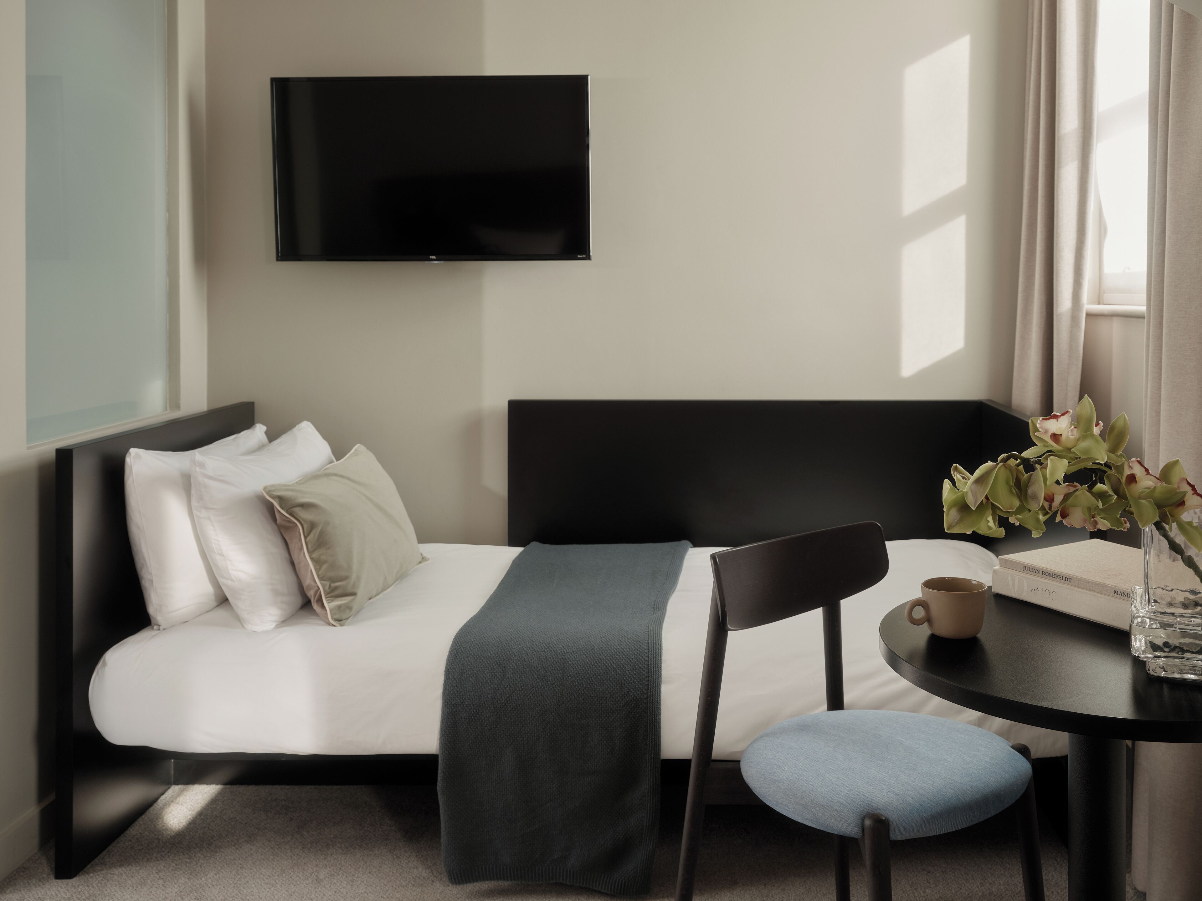 Quarto de hotel moderno com cama, escrivaninha, cadeira, televisão de tela plana e janela com cortinas.