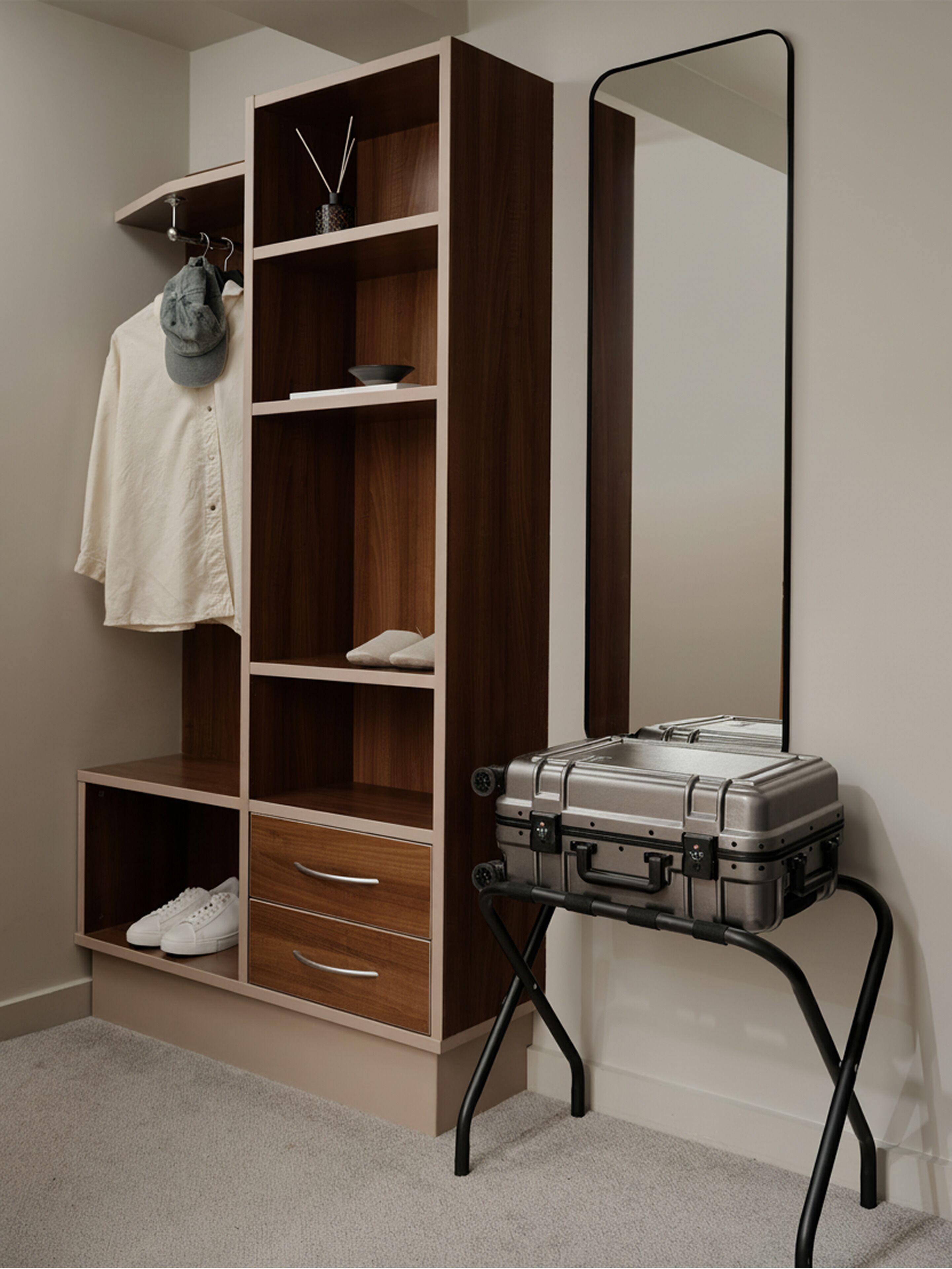 A room with a wardrobe, a mirror, and a suitcase on a stand.