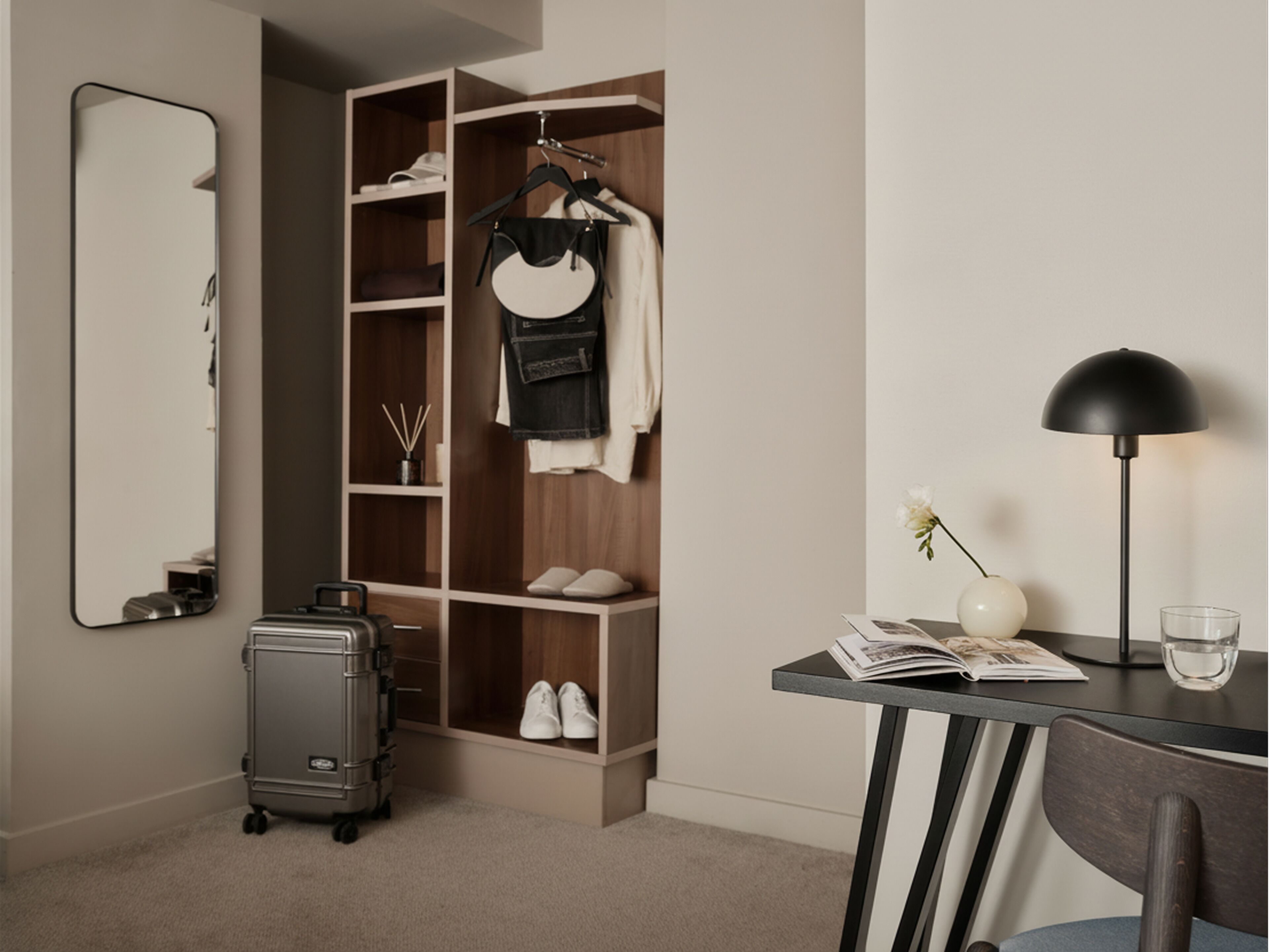 Quarto moderno com guarda-roupa, escrivaninha com luminária, mala e espelho.