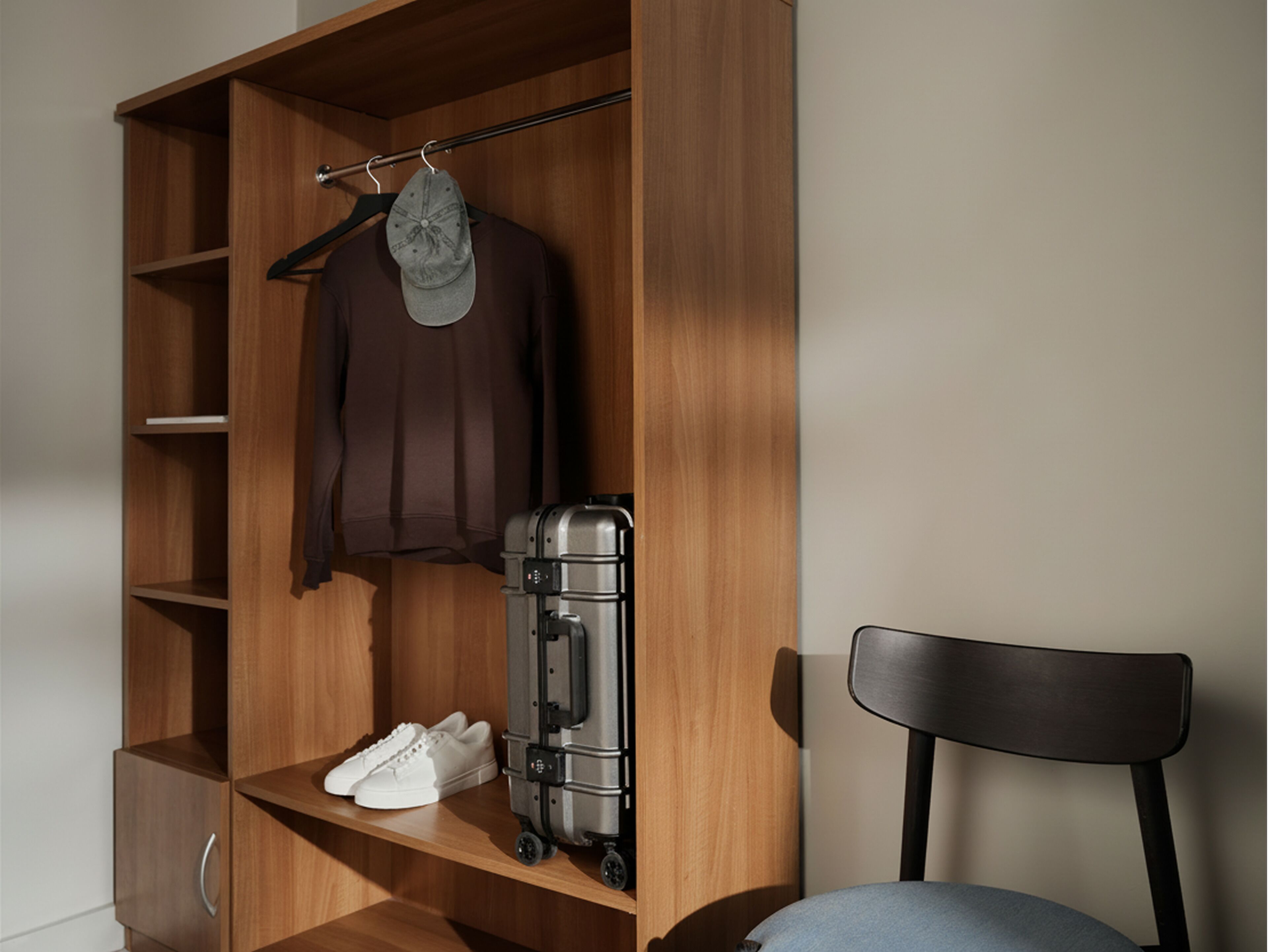 Een houten garderobe met planken, een kledingroede en een stoel.