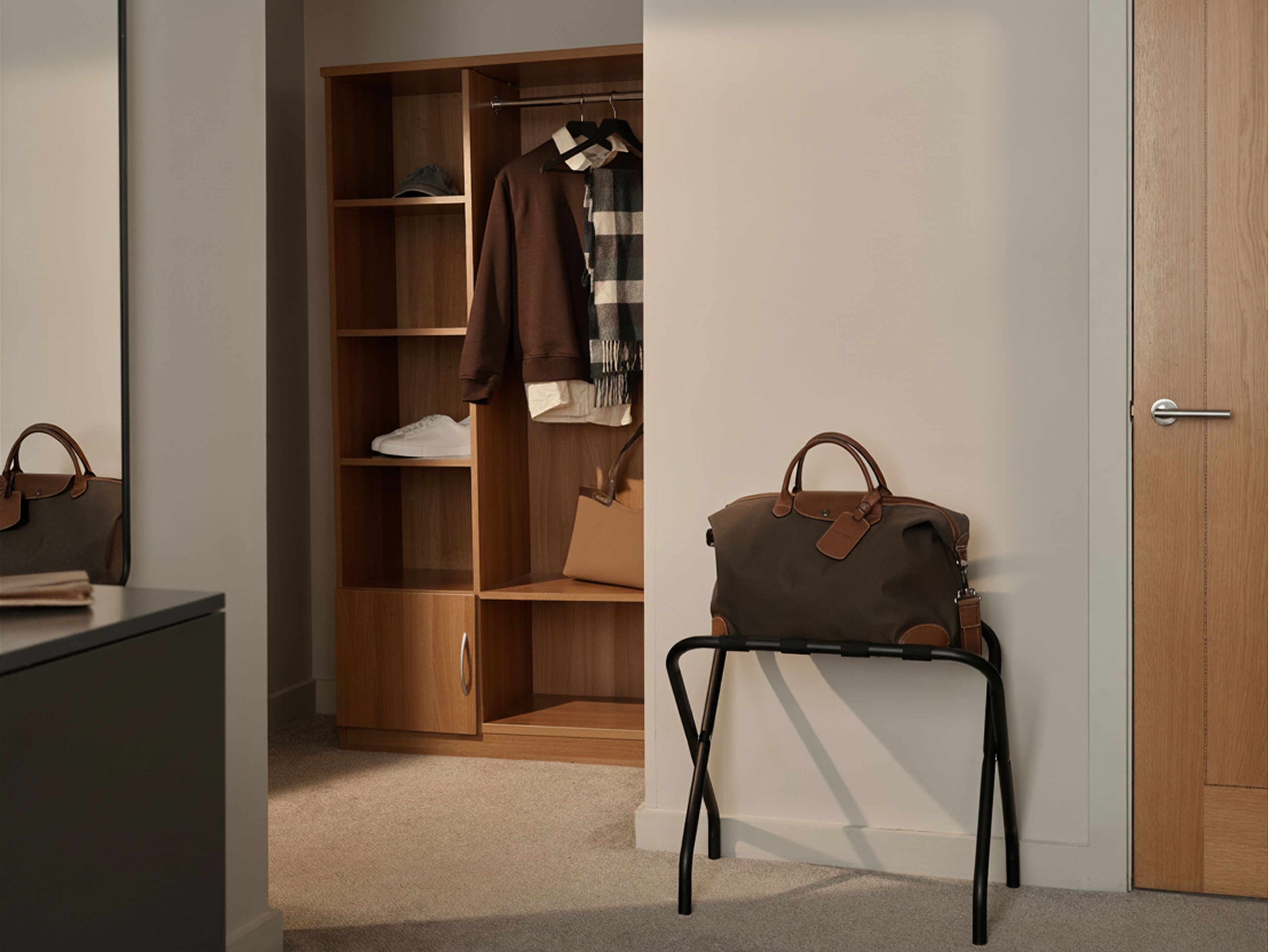 A room with a wooden wardrobe, a small table with a handbag, and a door.